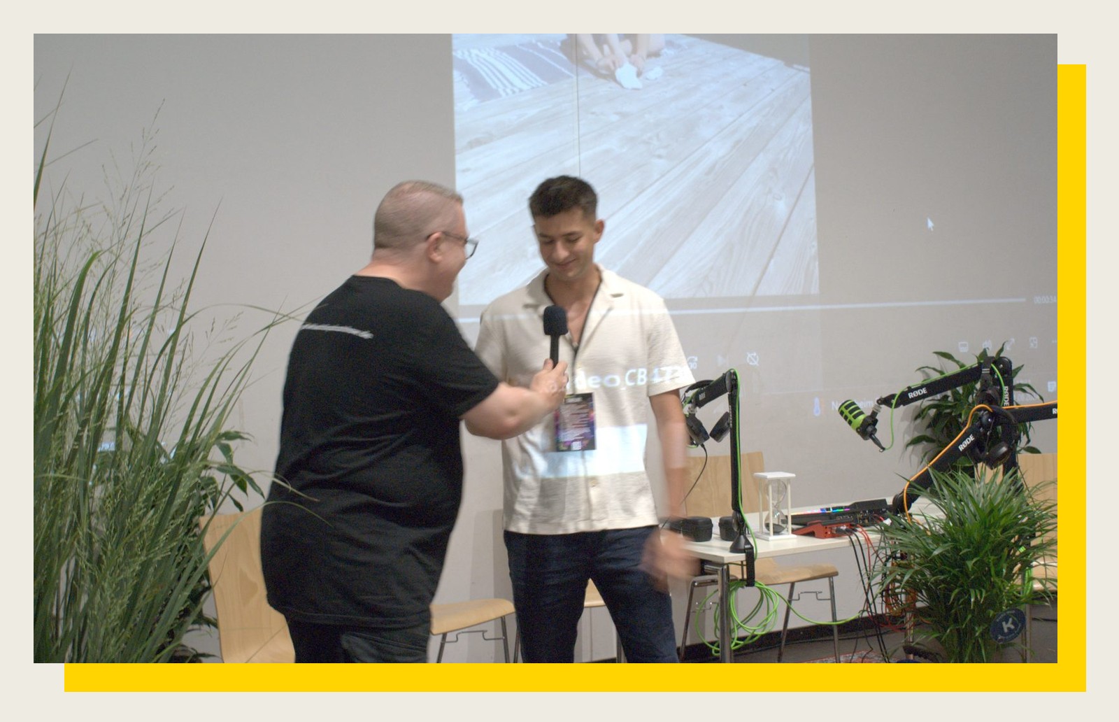 Ein Moderator interviewt mit Mikrofon einen Gast auf der Festivalbühne vor einer Leinwand