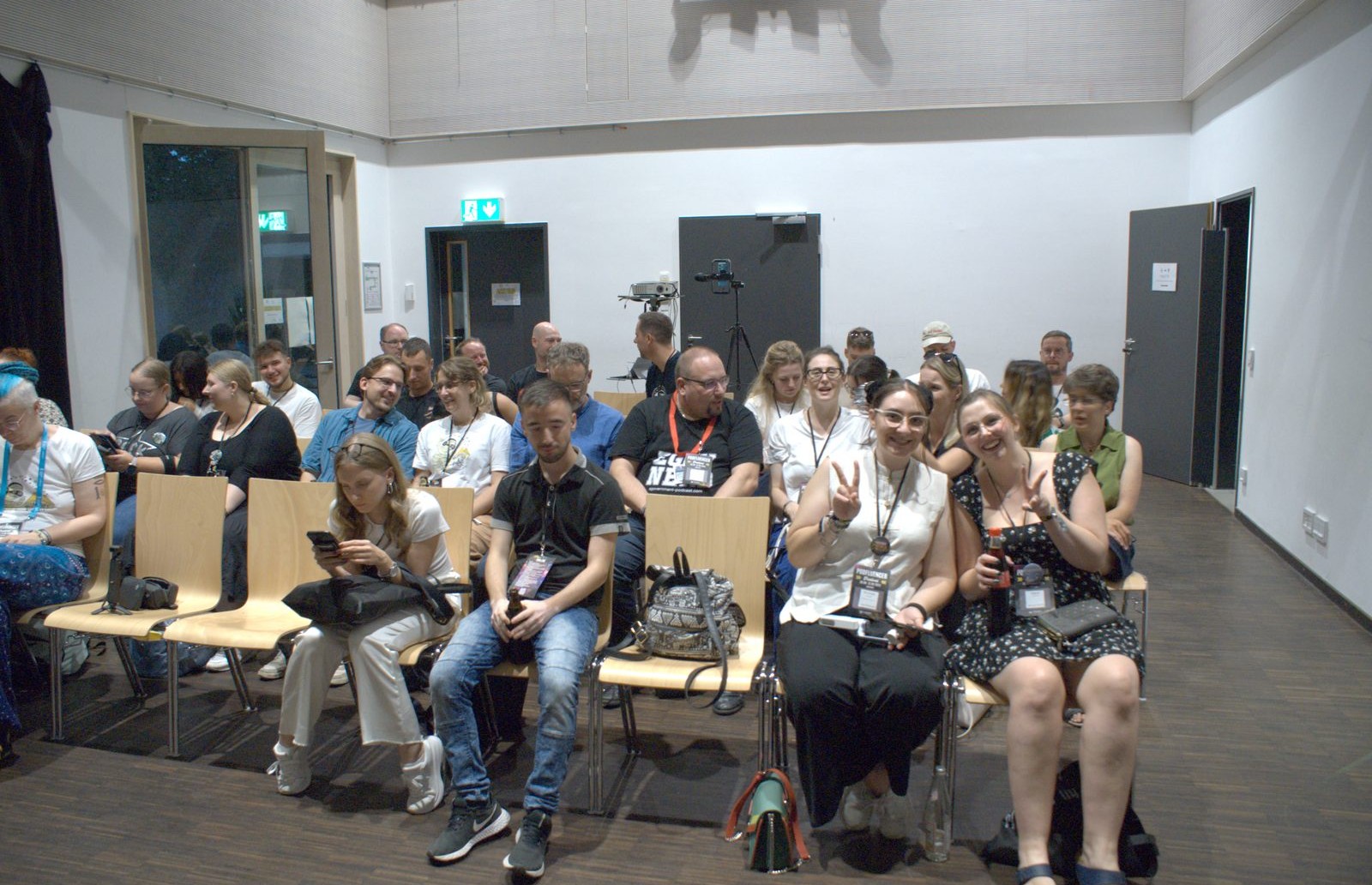 Publikum im Saal beim Podfluencer Festival, zwei Besucherinnen zeigen lachend das Victory-Zeichen